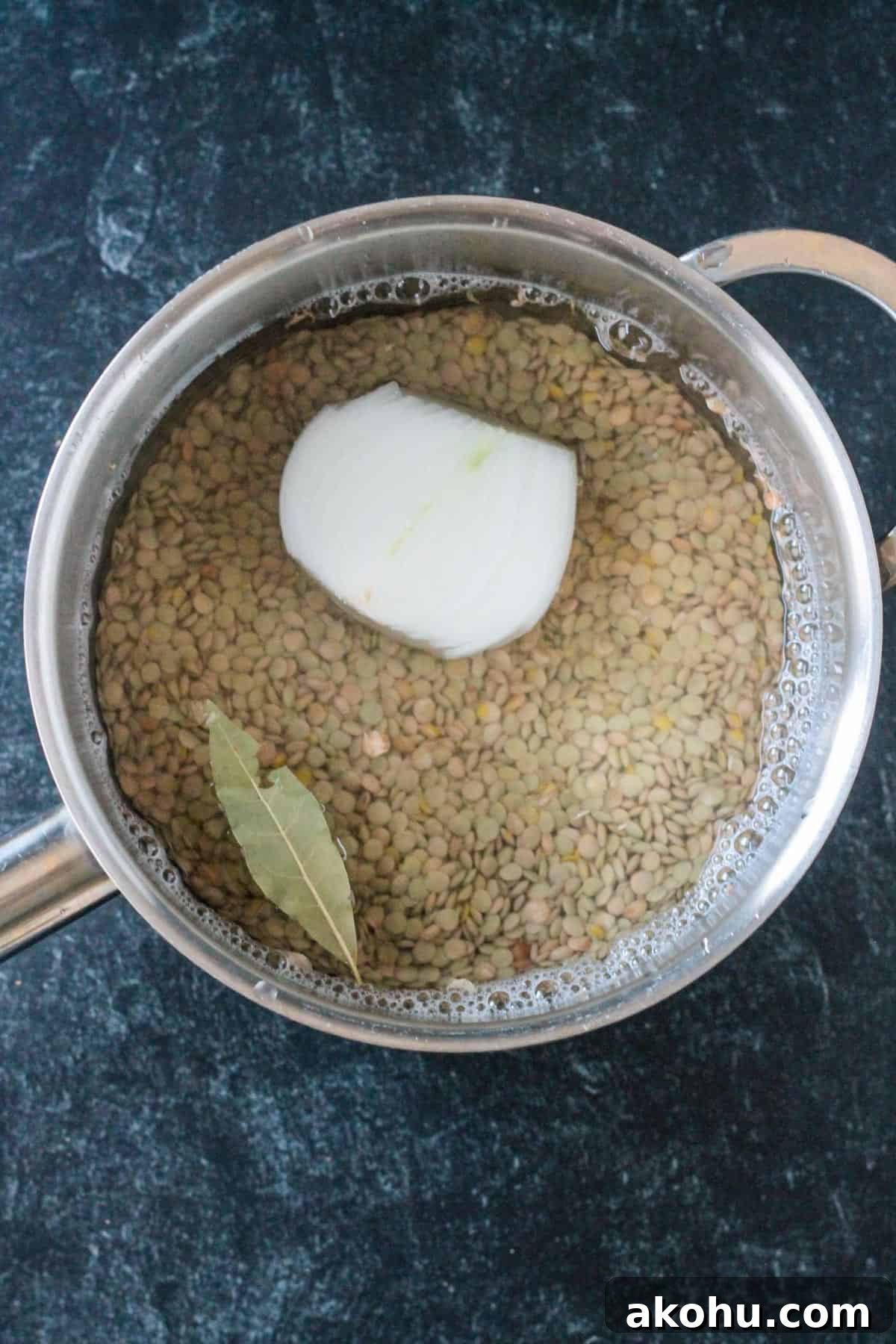Uncooked lentils in a pot with water, onion, and a bay leaf.