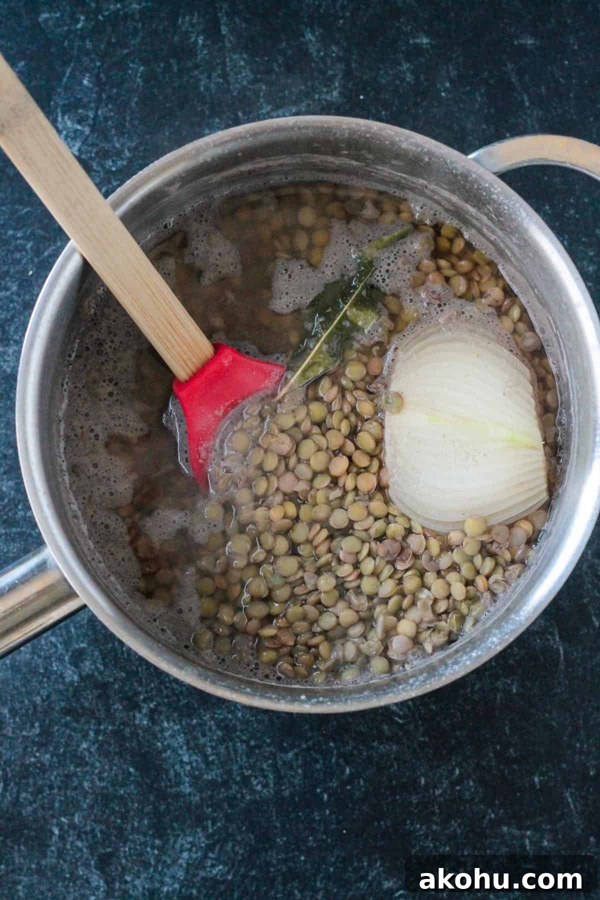 Cooked lentils in a pot with onion and a bay leaf.