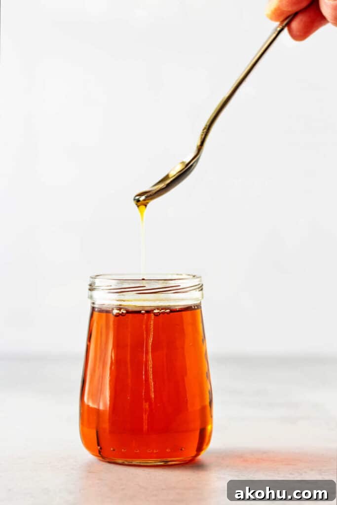 I small, clear glass jar full of amber liquid with a spoon held over the jar drizzling some back down into it.