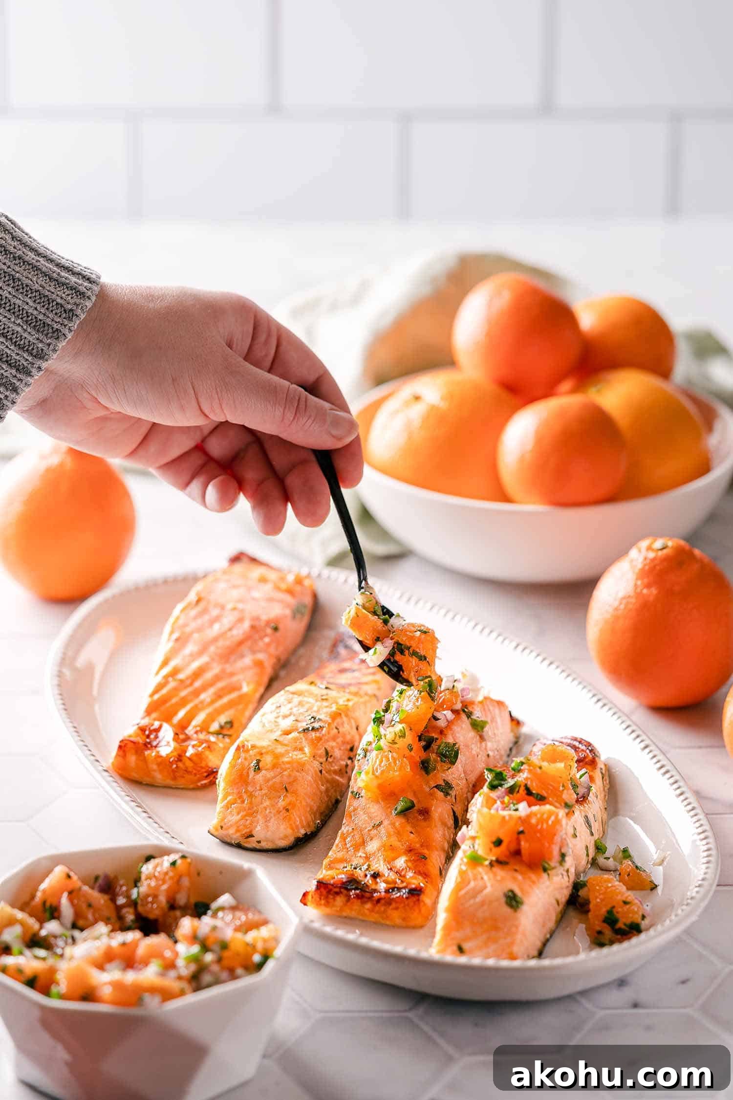 Citrus-Herb Salmon with Orange and Red Onion Salsa 10 hand spooning orange salsa over broiled salmon on platter
