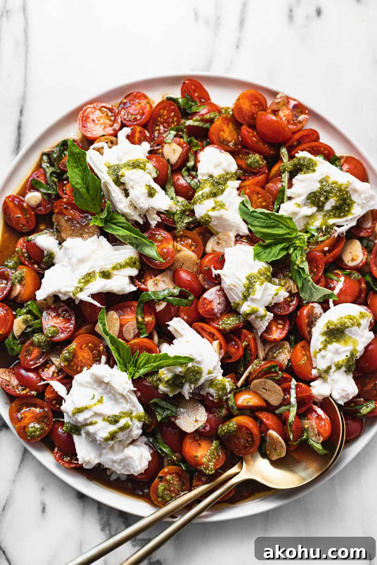 Large white plate with sliced tomatoes and burrata salad garnished with pesto.