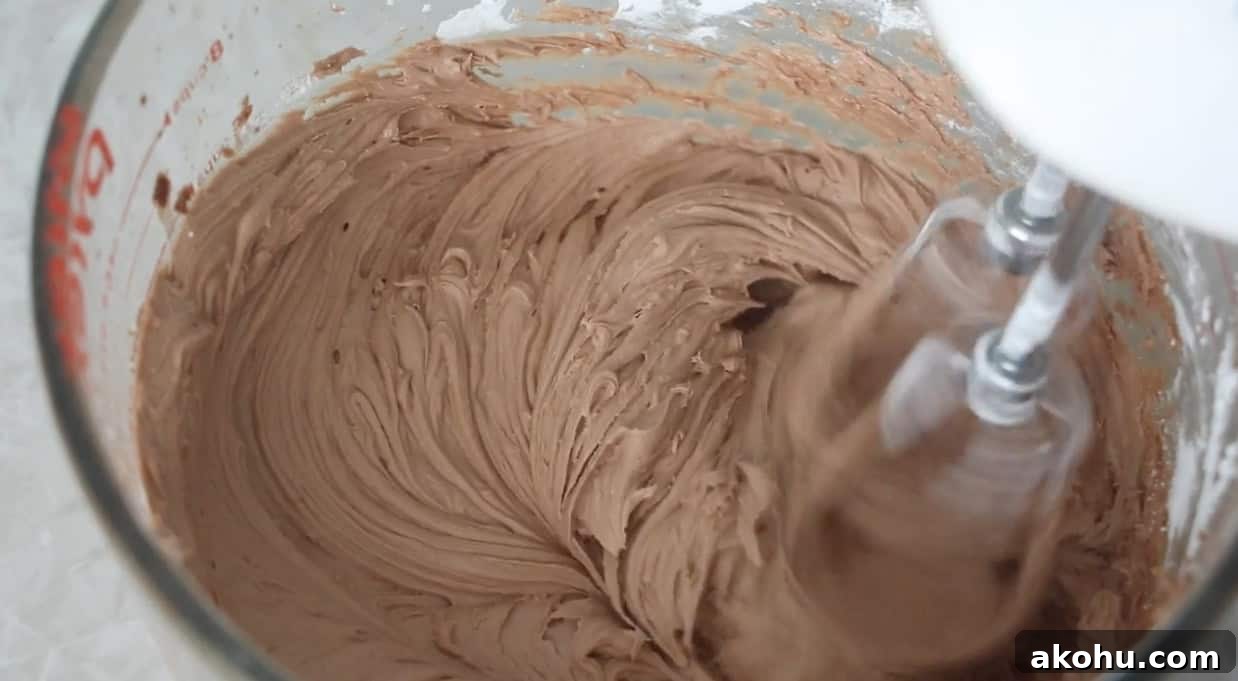 Ultimate Texas Sheet Cake Recipe for Rich Chocolate Dessert 10 Glass mixing bowl of chocolate frosting beat with electric mixer.