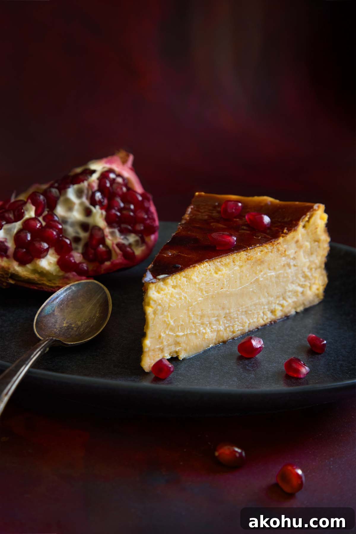 Basque Cheesecake with Tangy Pomegranate Molasses Glaze 2 A slice of burnt Basque cheesecake with pomegranate on a plate, garnished with pomegranate seeds and a spoon.