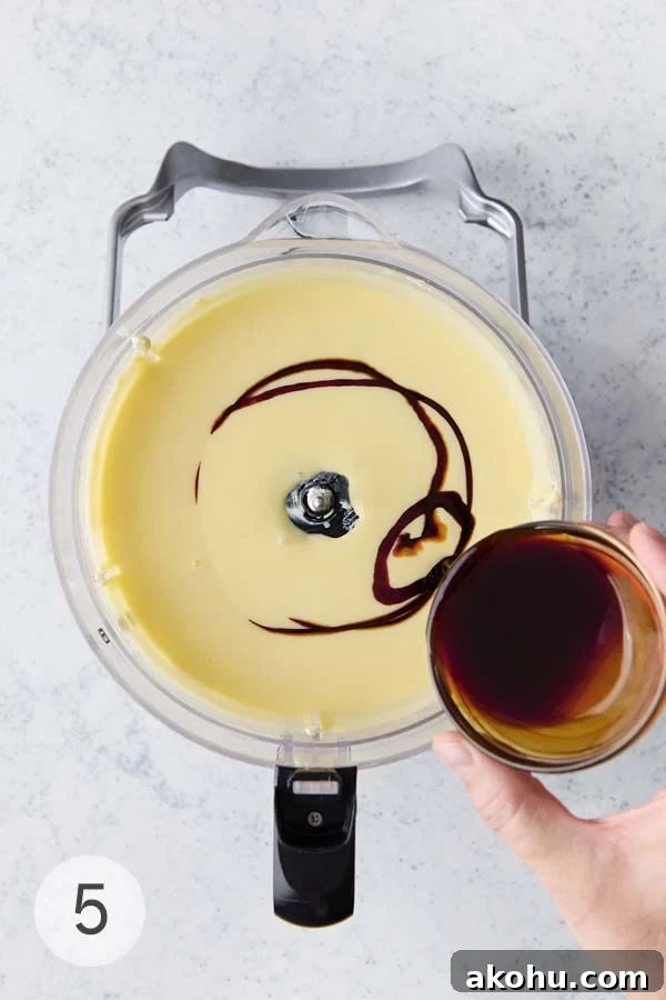 Basque Cheesecake with Tangy Pomegranate Molasses Glaze 11 Pomegranate molasses being poured into a food processor filled with basque cheesecake recipe batter.