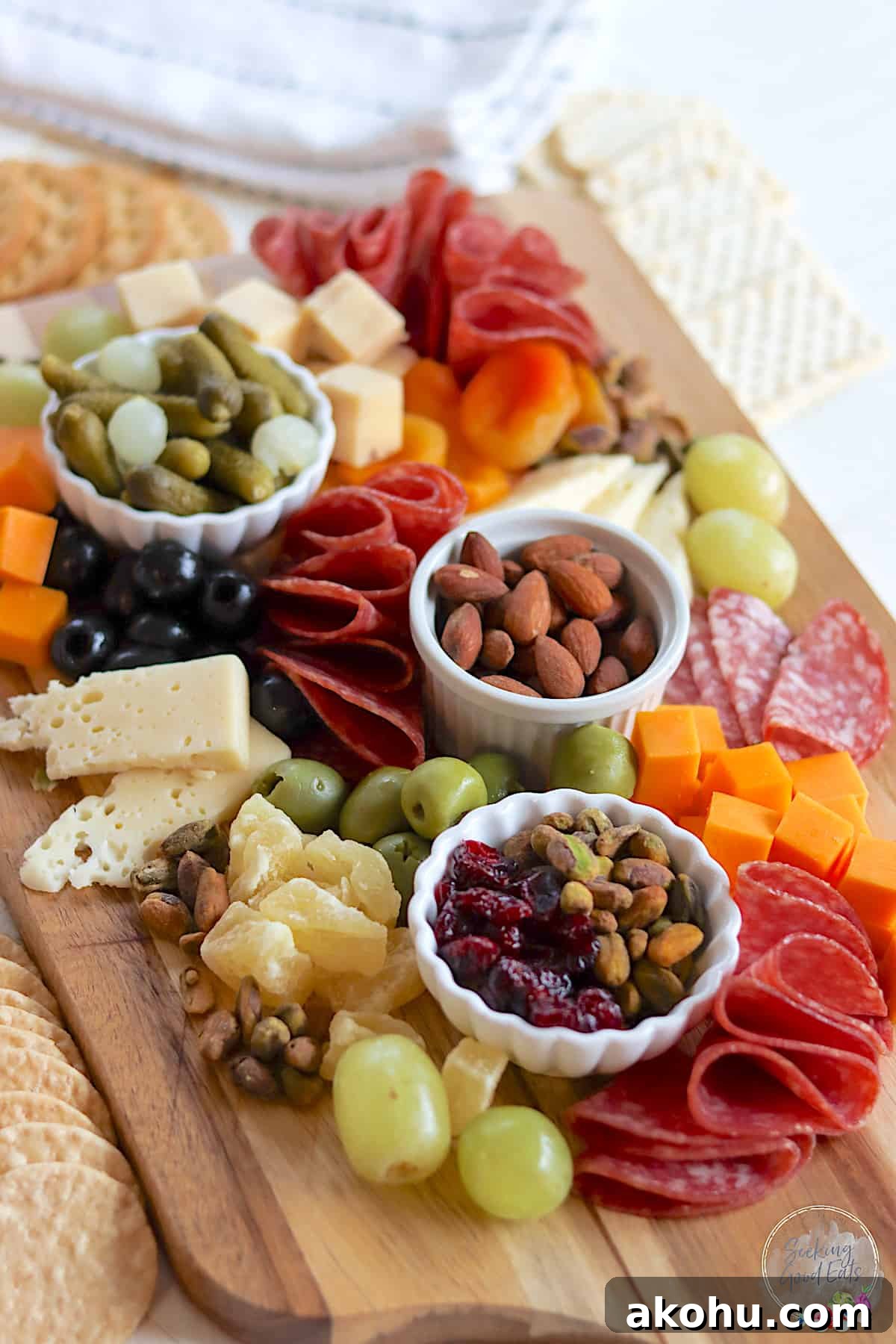 A rectangle wooden board with a variety of colors and textures of cheeses, salami, dried fruits, nuts, and crackers.