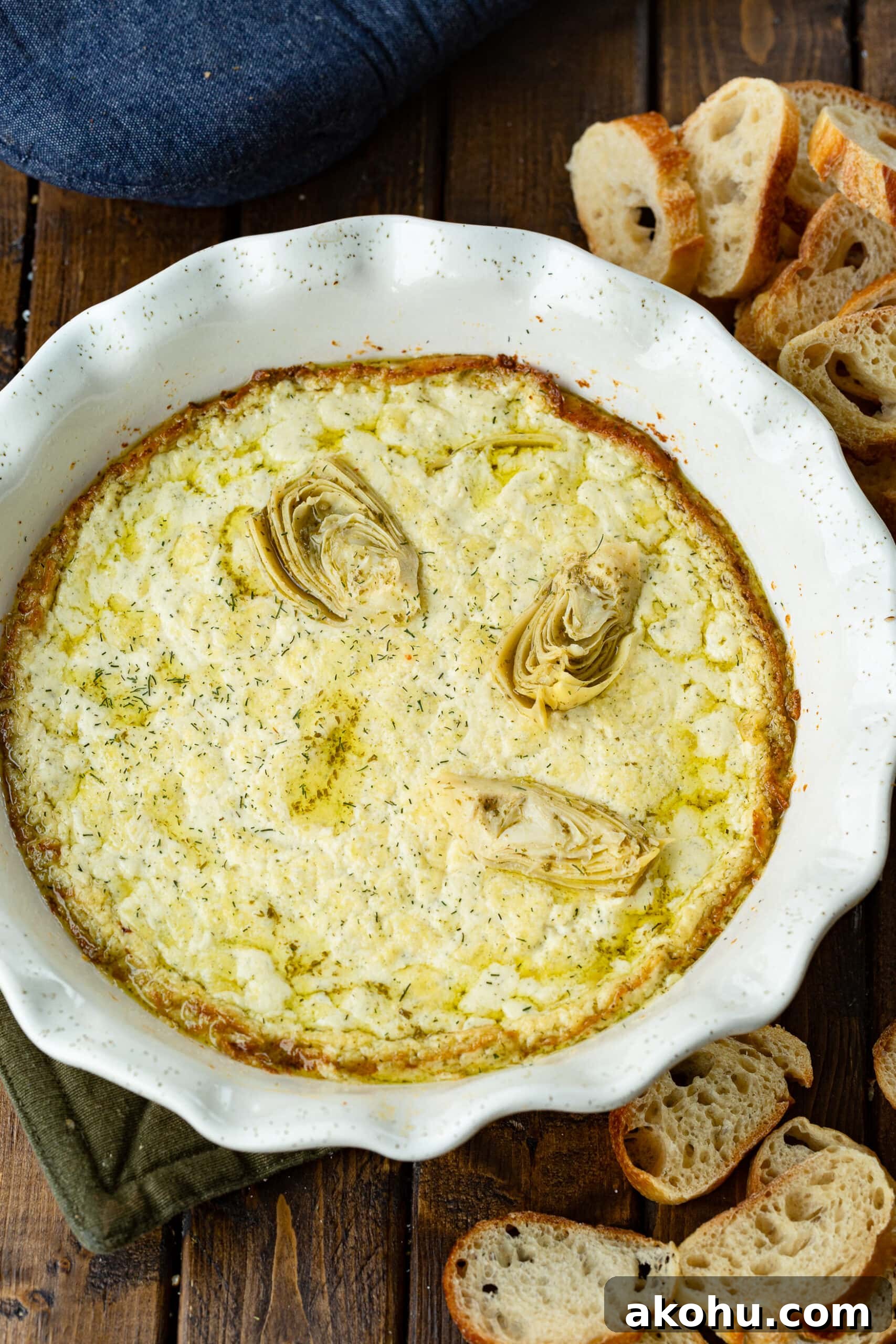 a white ceramic circular baking dish full of golden creamy artichoke dip with several pieces of artichoke placed on top.