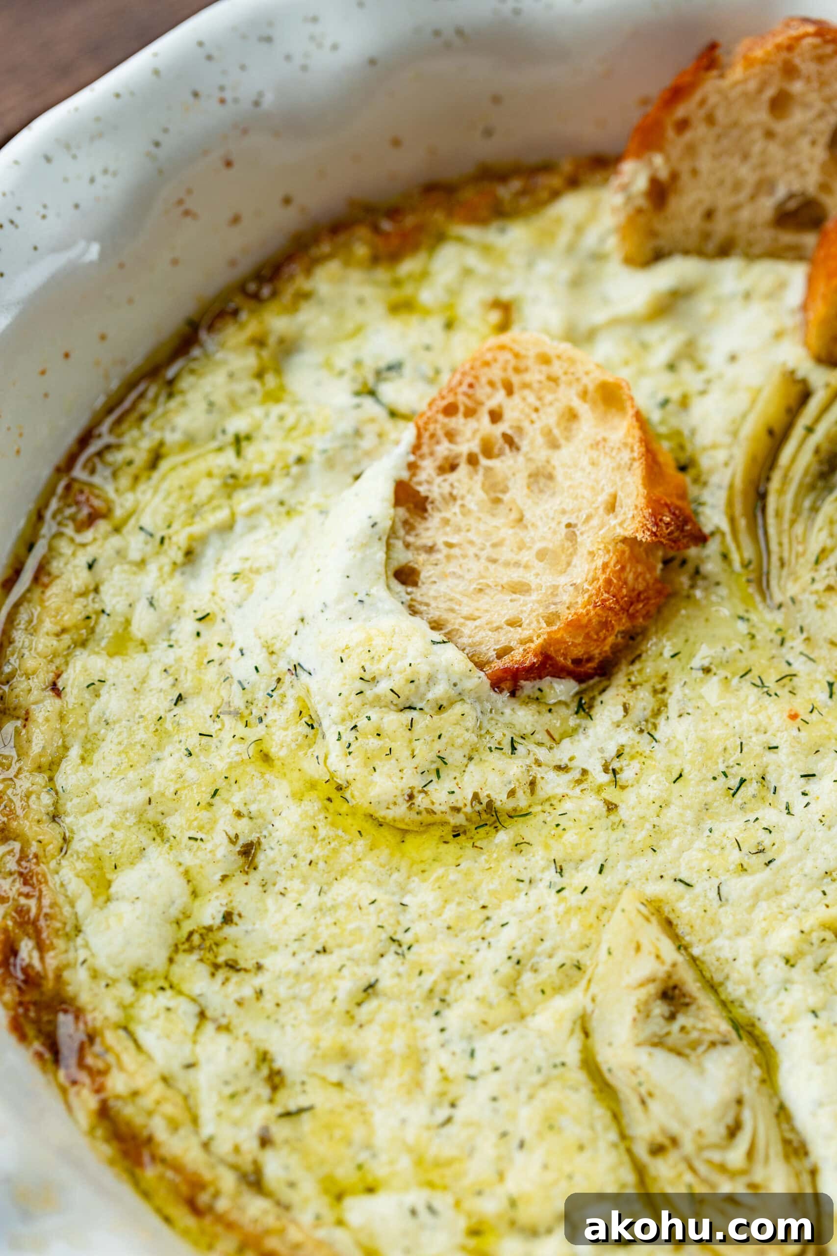 a single baguette slice stuck into a large dish of creamy artichoke dip.