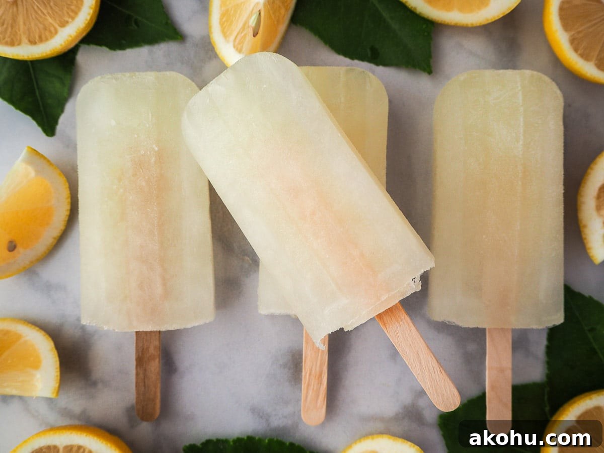 Row of three lemonade popsicles with a forth stacked on top, surrounded by fresh lemon slices and lemon leaves.