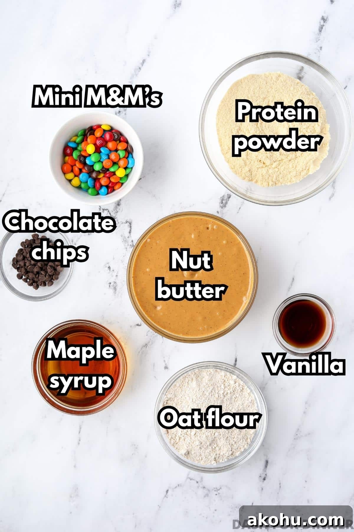 Monster Cookie Protein Bars: Chewy Peanut Butter Oat Bars 3 An overhead view of different bowls with different ingredients, including: nut butter, protein powder, mini M&m's, chocolate chips, maple syrup, etc.