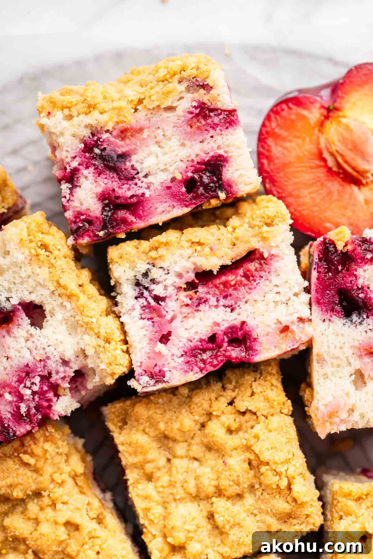 Classic Plum Cake Recipe: Moist, Fragrant Holiday Dessert 2 Slices of plum cake with streusel on a platte with a half plum nearby.
