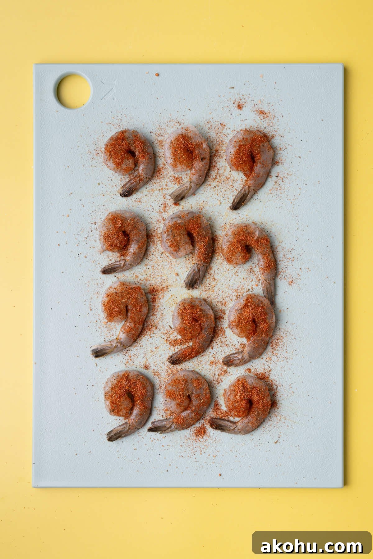 30-Min Cajun Creamy Shrimp Pasta Recipe 4 Raw shrimp lined up on a chopping board with Cajun season covering both sides.