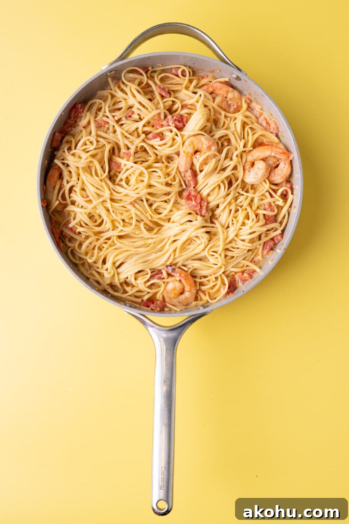 30-Min Cajun Creamy Shrimp Pasta Recipe 6 Tossing pasta in a creamy Cajun sauce made in a pan with shrimp.