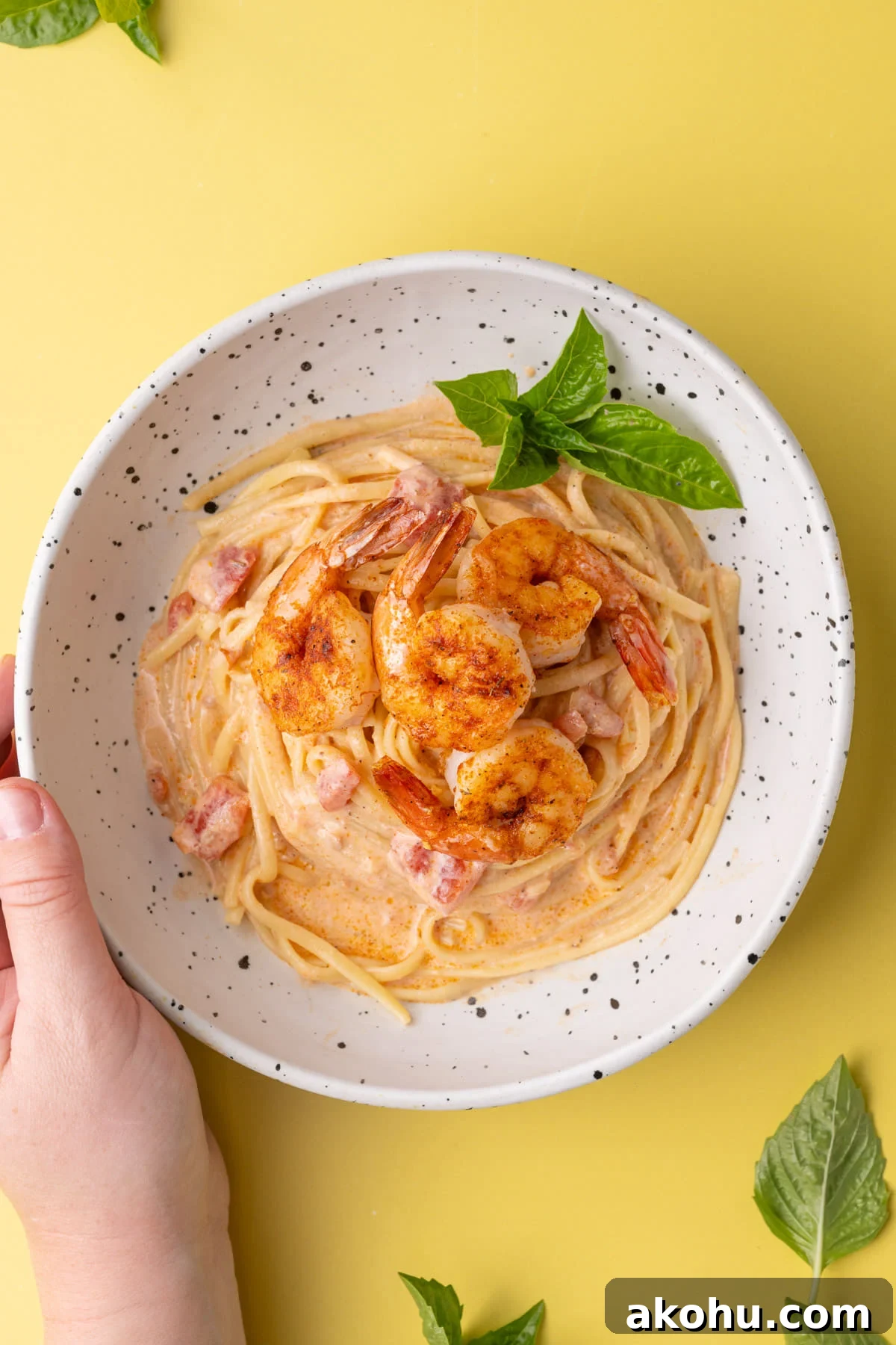 30-Min Cajun Creamy Shrimp Pasta Recipe 7 Plated creamy Cajun pasta with shrimp in a shallow bowl with hand cupping the bowl.