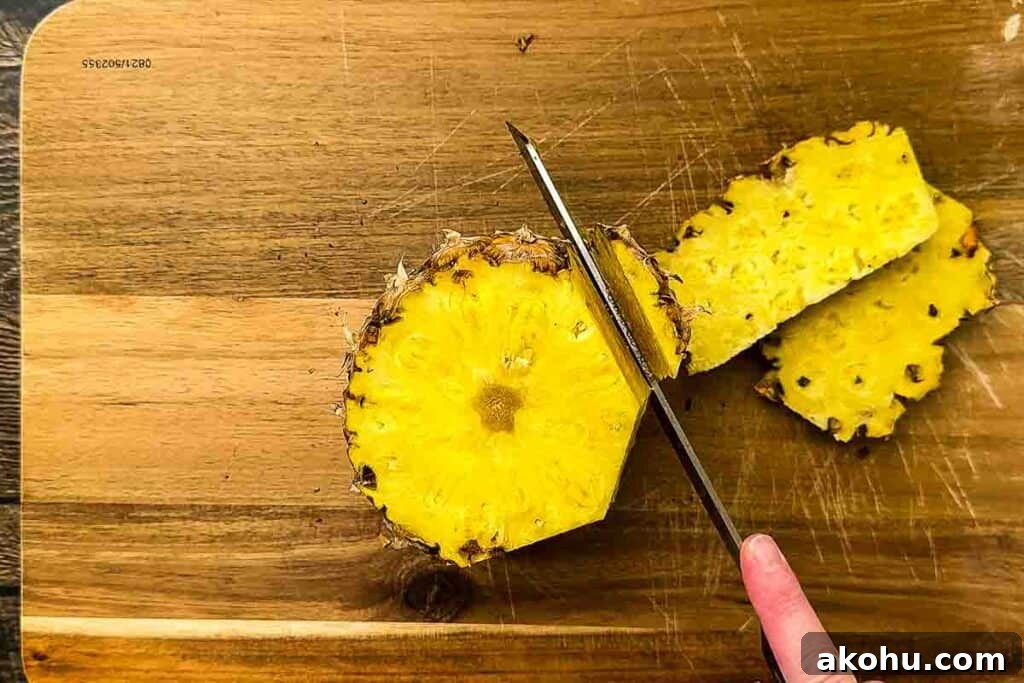 A whole pineapple with the top and bottom cut off, standing upright, with the outer skin being sliced off with a knife.