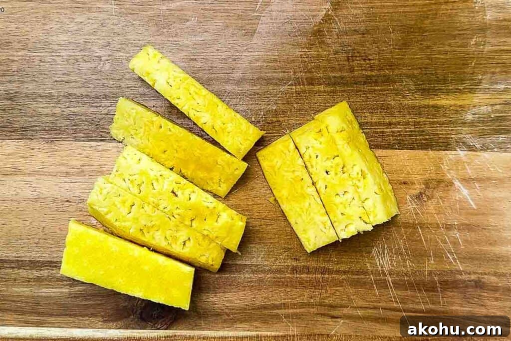 Pineapple cut into 1-inch thick spears on a cutting board.