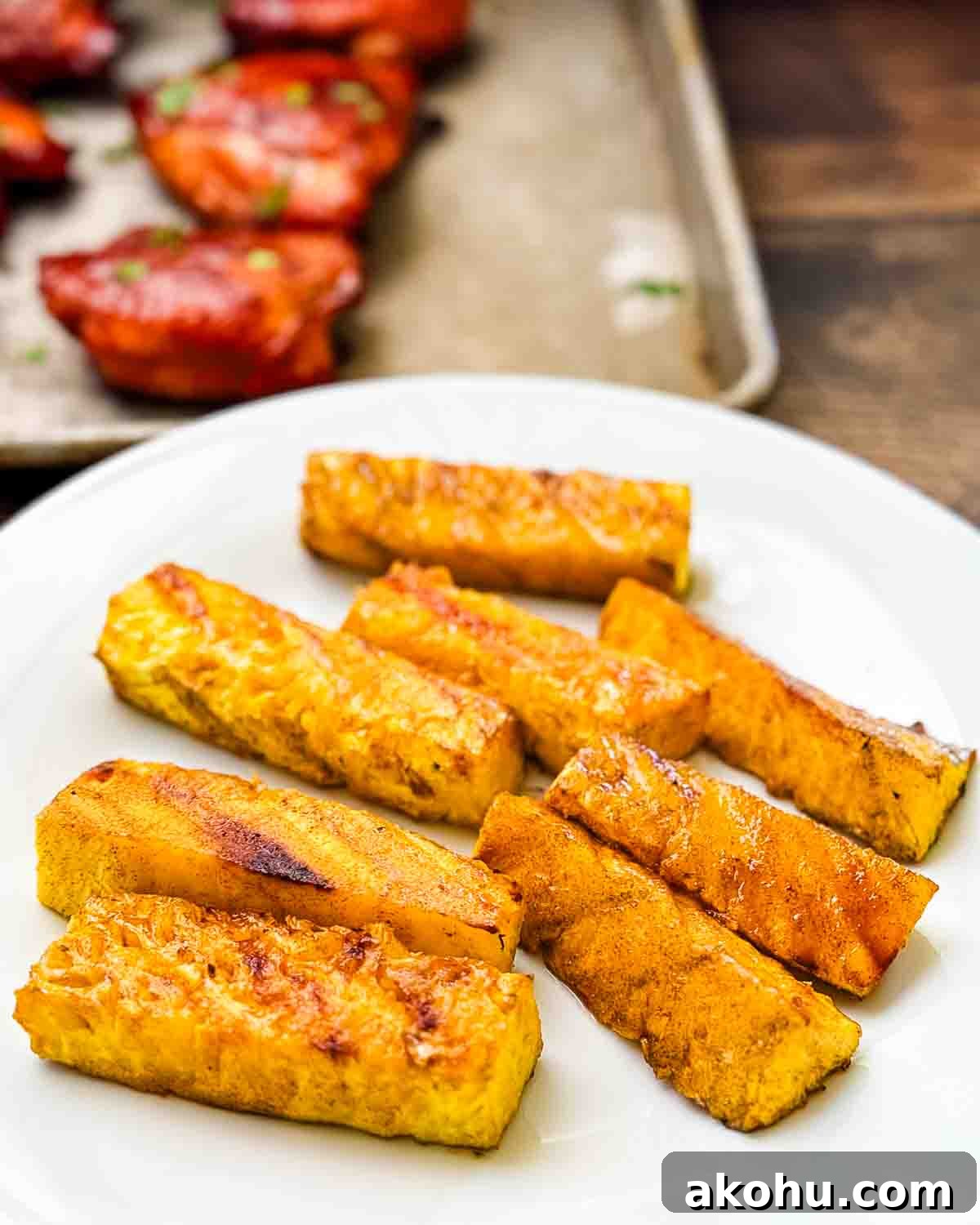 Smoked pineapple spears served alongside smoked huli huli chicken on a wooden table.