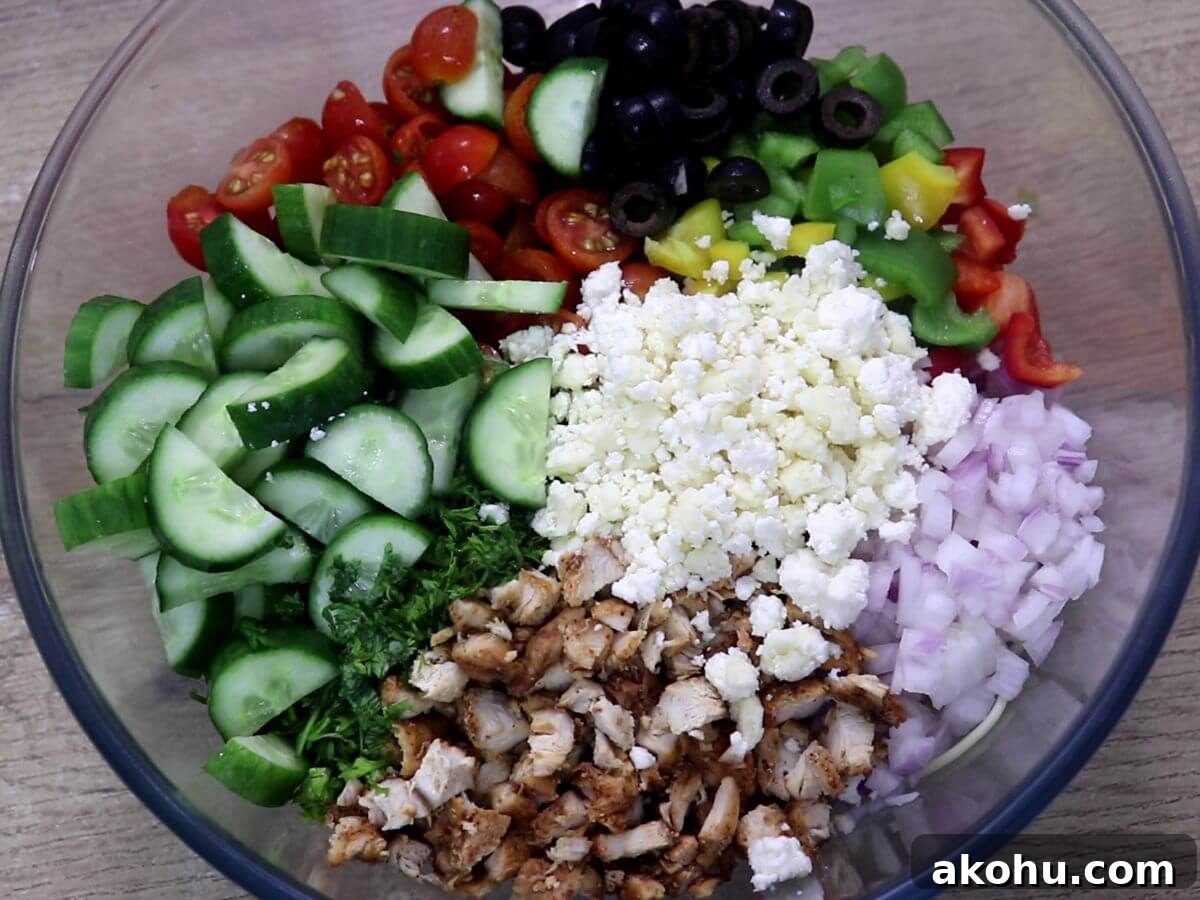 A mixing bowl containing spaghetti salad with colorful vegetables, chicken and feta cheese.