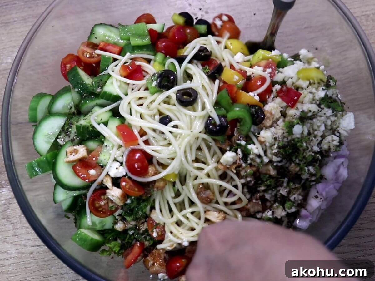 Close-up of a vibrant spaghetti salad being mixed with dressing.
