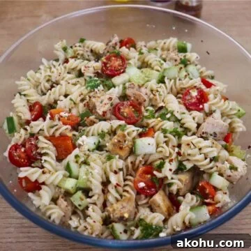 Greek chicken pasta salad in a large bowl with feta cheese and vegetables.
