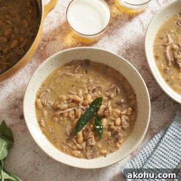 A Dutch oven and two bowls of pork stew, two glasses of beer, some fresh sage, and a blue napkin.