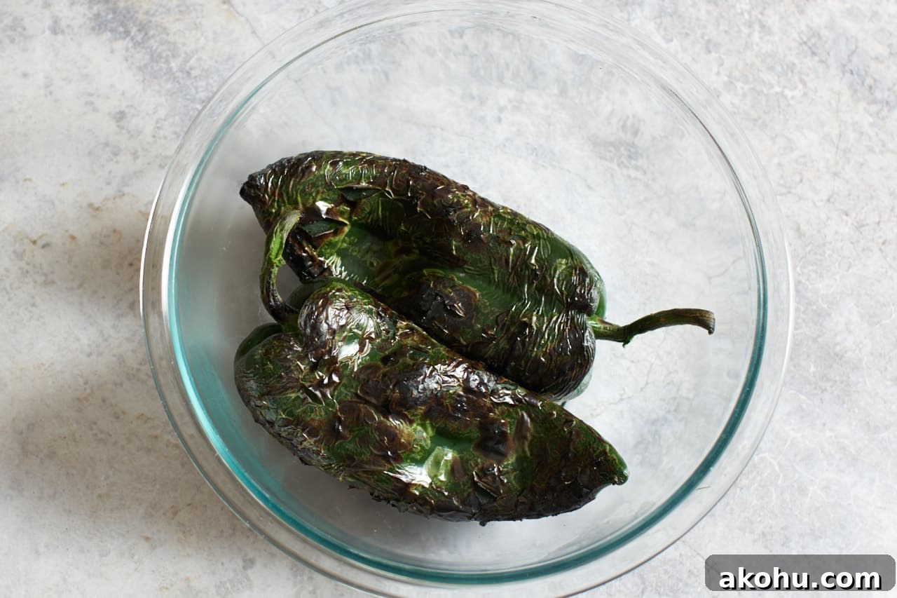Two roasted poblano peppers in a glass bowl.