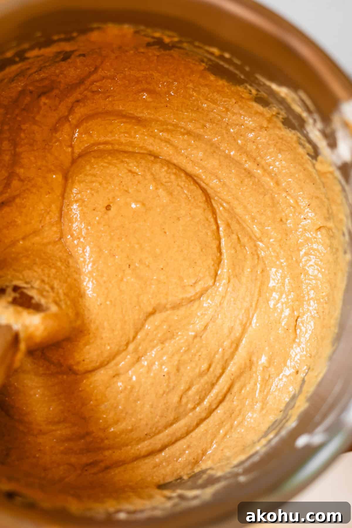 Thick, creamy, light brown batter being mixed in a metal bowl with a wooden spoon, likely for baking bread or cake.