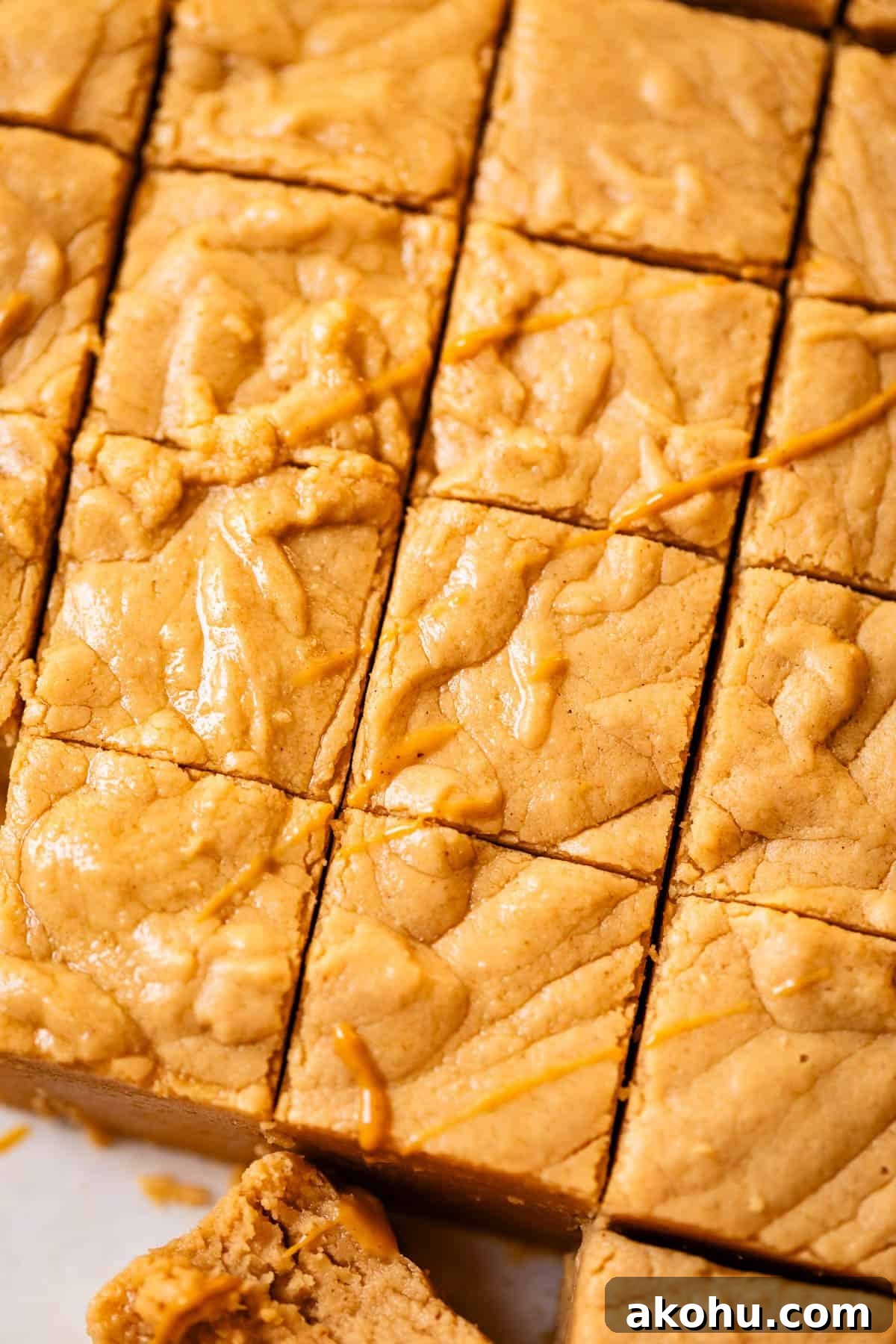 Close-up of soft, golden peanut butter fudge cut into squares, with a smooth, slightly textured surface and a light drizzle of peanut butter on top. One bar at the bottom is slightly pulled out.
