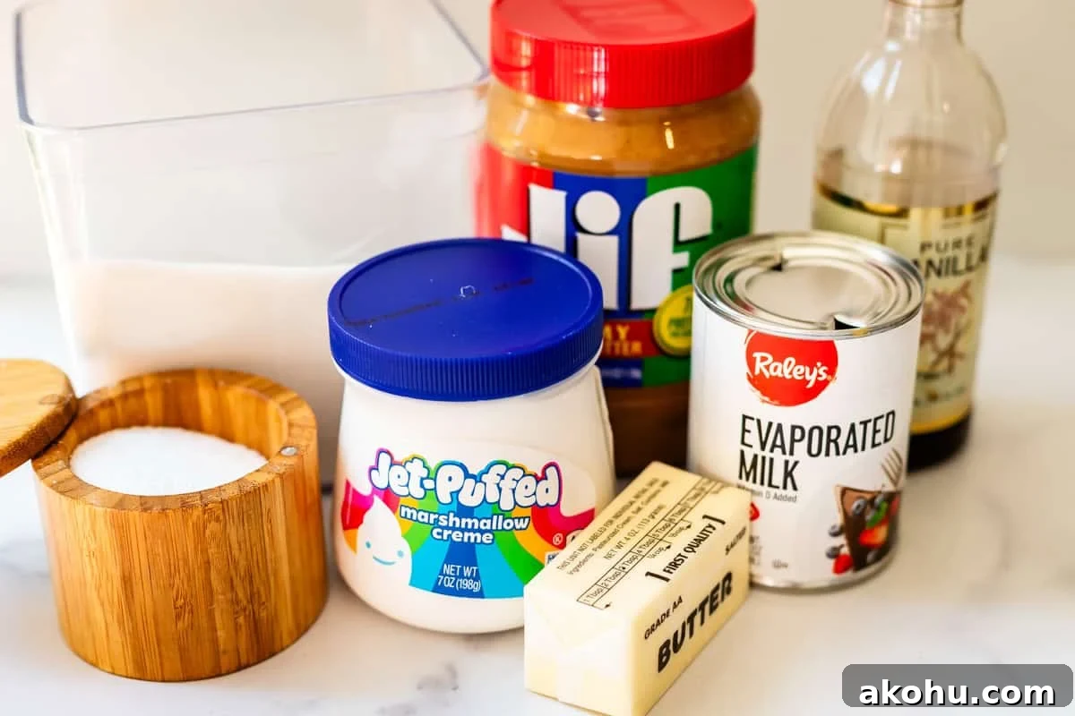 A collection of baking ingredients on a counter: a container of sugar, a wooden salt box, a jar of peanut butter, vanilla extract, Jet-Puffed marshmallow creme, a can of evaporated milk, and a stick of butter.