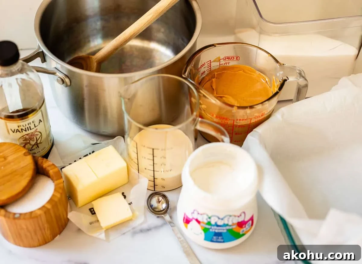 Ingredients and tools for making fudge: a saucepan, wooden spoon, vanilla extract, butter, sugar, measuring cups with cream and peanut butter, marshmallow creme, and a parchment-lined baking dish on a countertop.