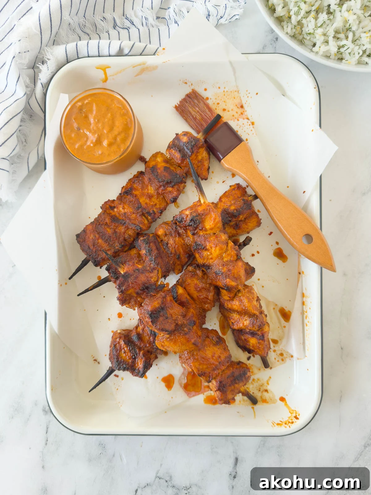 A tray of bright orange harissa chicken skewers with a harissa sauce and pastry brush.