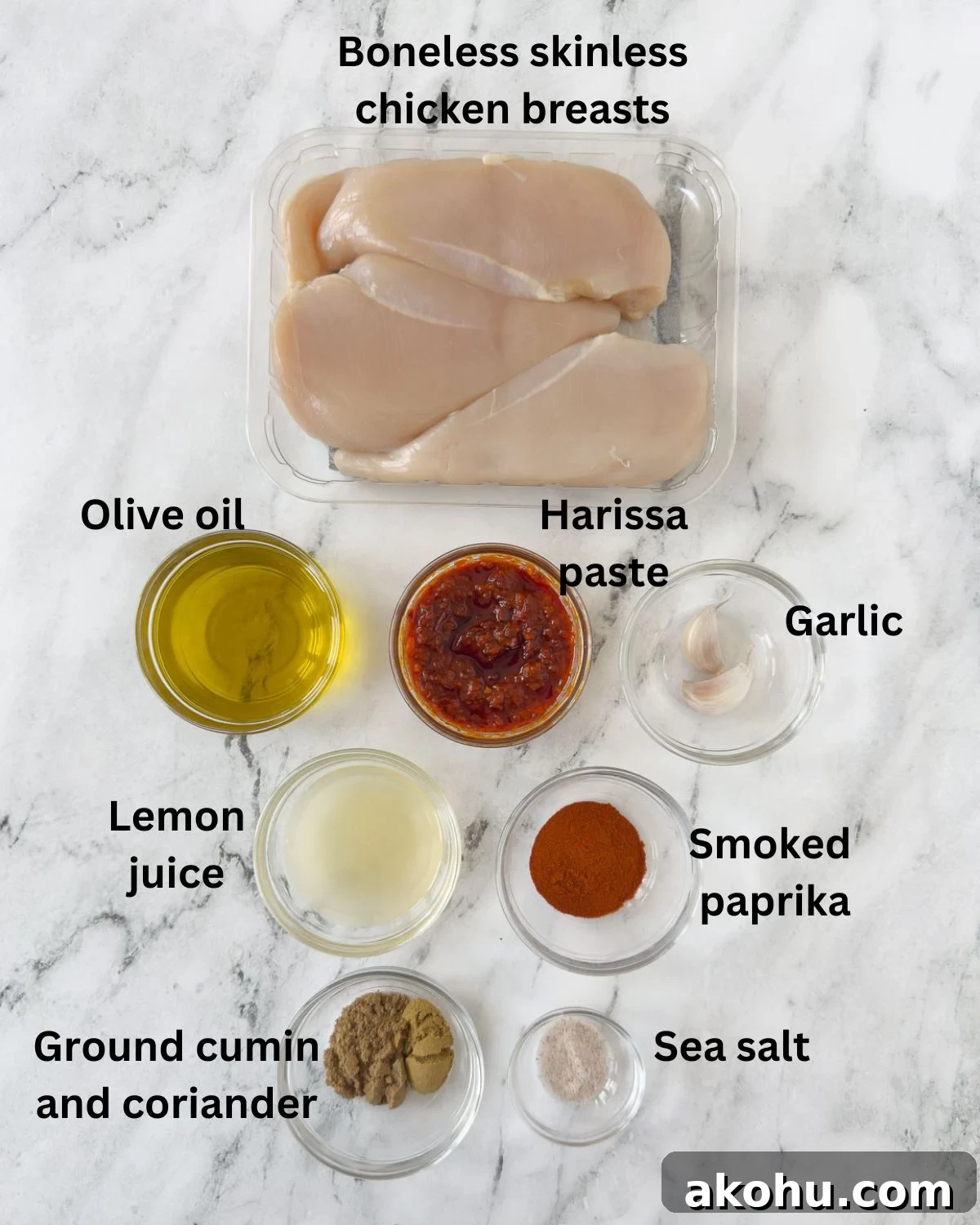 Ingredients for harissa chicken in prep bowls on a marble counter.