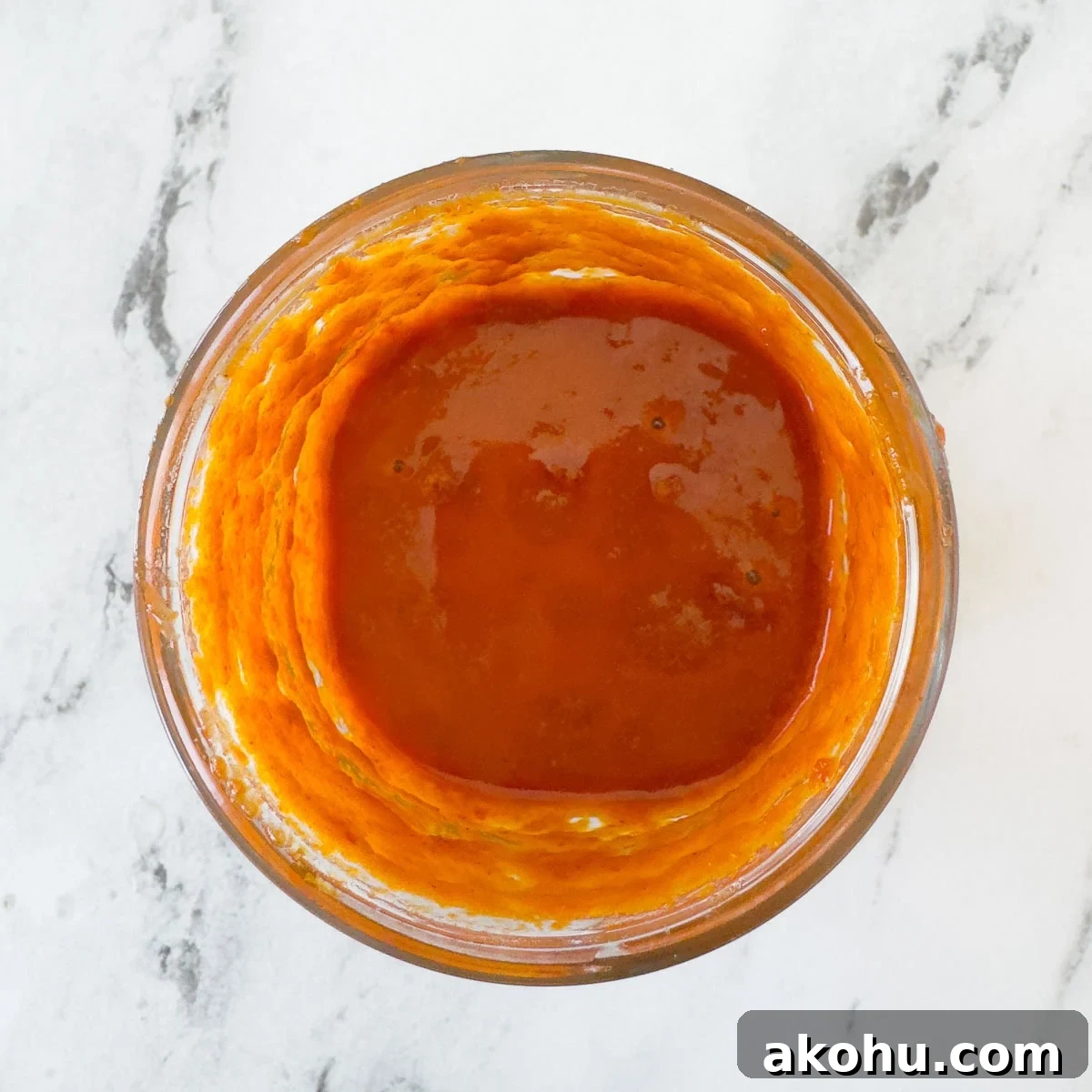 Bright orange red harissa marinade in a glass jar.