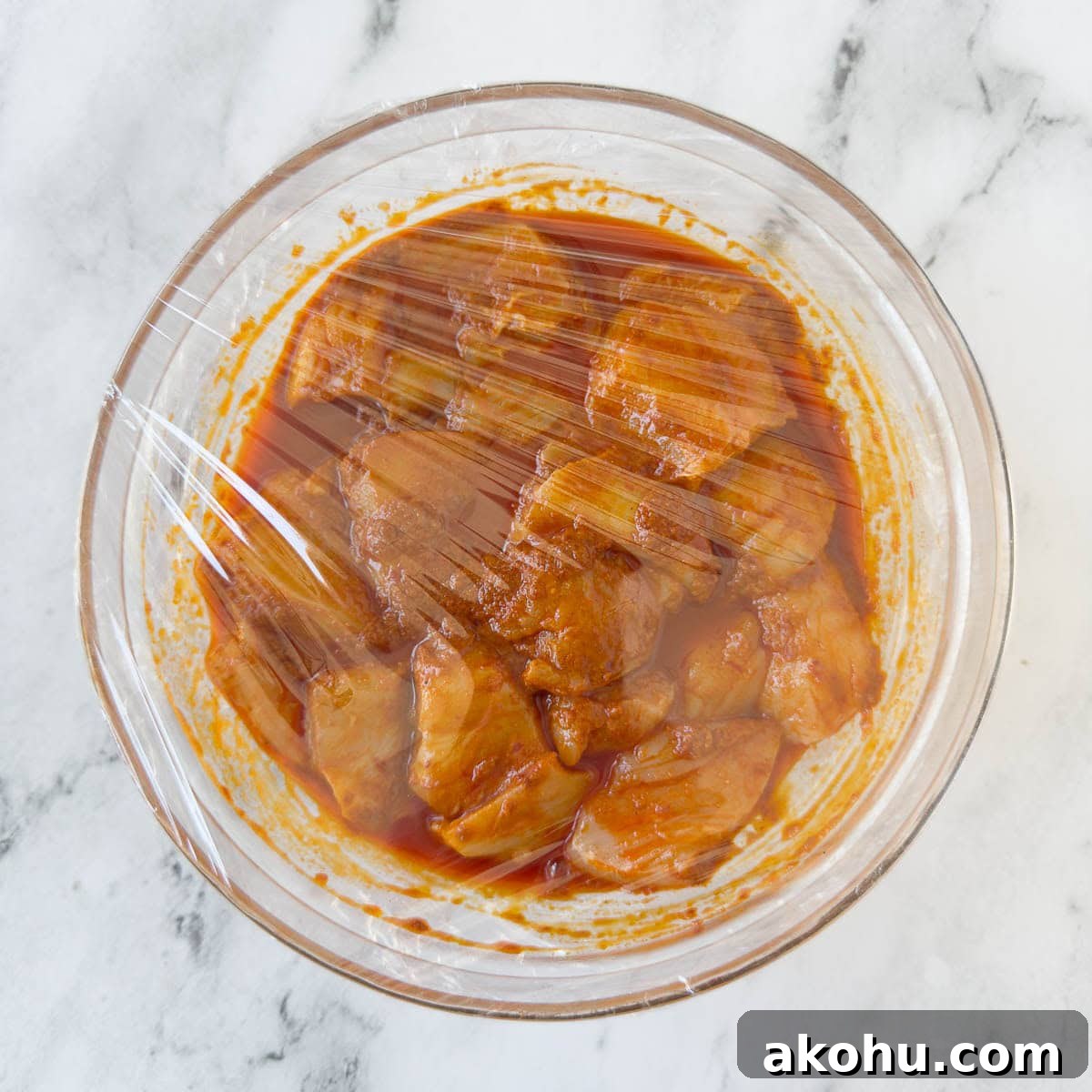Covering a bowl of chicken in marinade  in plastic for resting in the refrigerator.