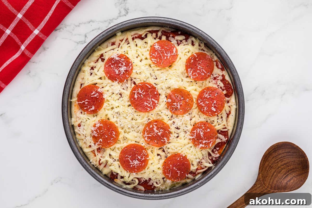 unbaked pizza in pan with shredded cheese and pepperoni toppings.