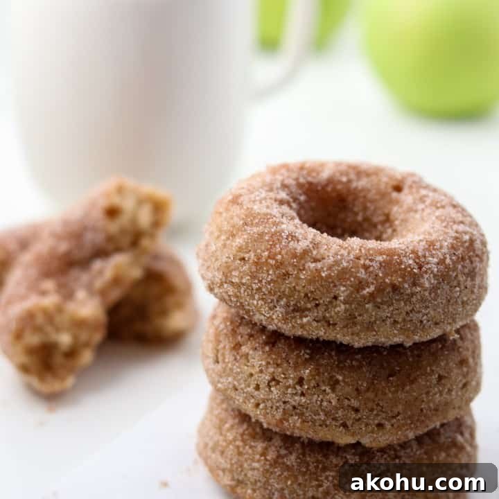 Close up of stack of three apple donuts next to a cup of coffee and apples