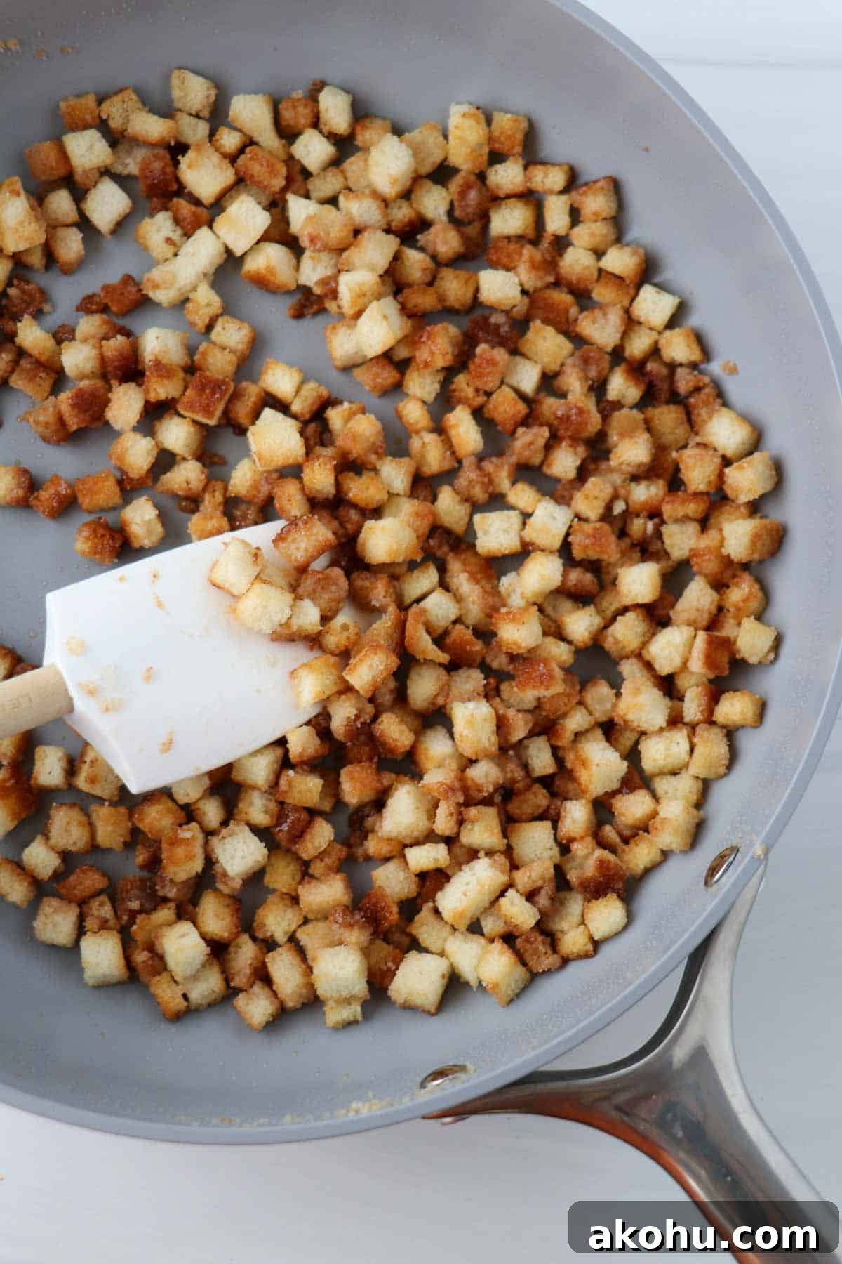 Caramelized bread cubes in a pan with a rubber spatula.