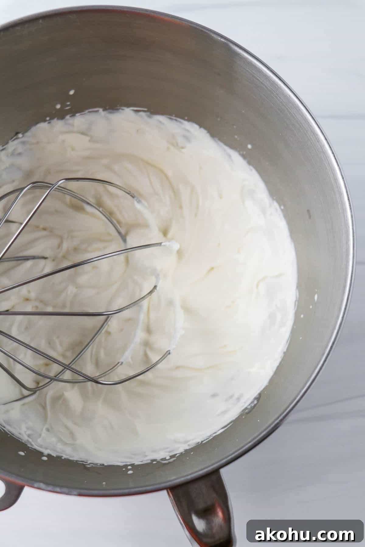 Whipped cream in a metal bowl with a whisk attachment.