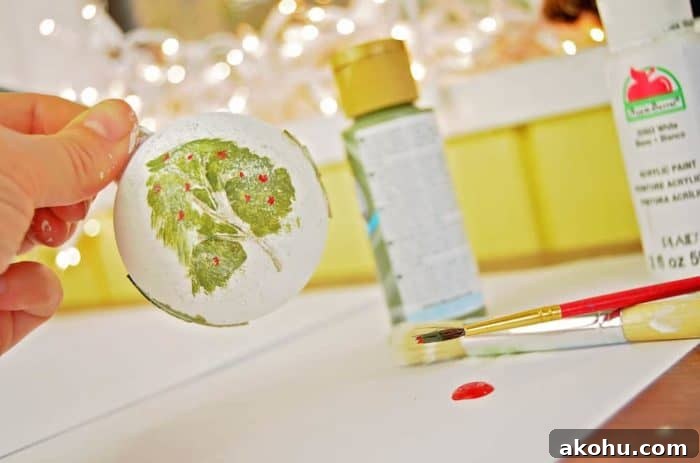 Photo shows a hand holding the ornament while red berries are being added to the tree