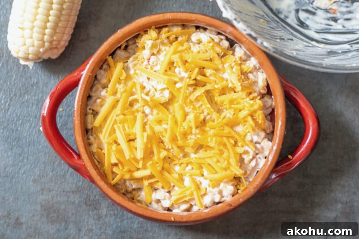Corn dip in red crock topped with shredded cheddar cheese.