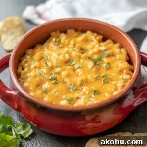 Warm corn dip in red bowl next to tortilla chips.