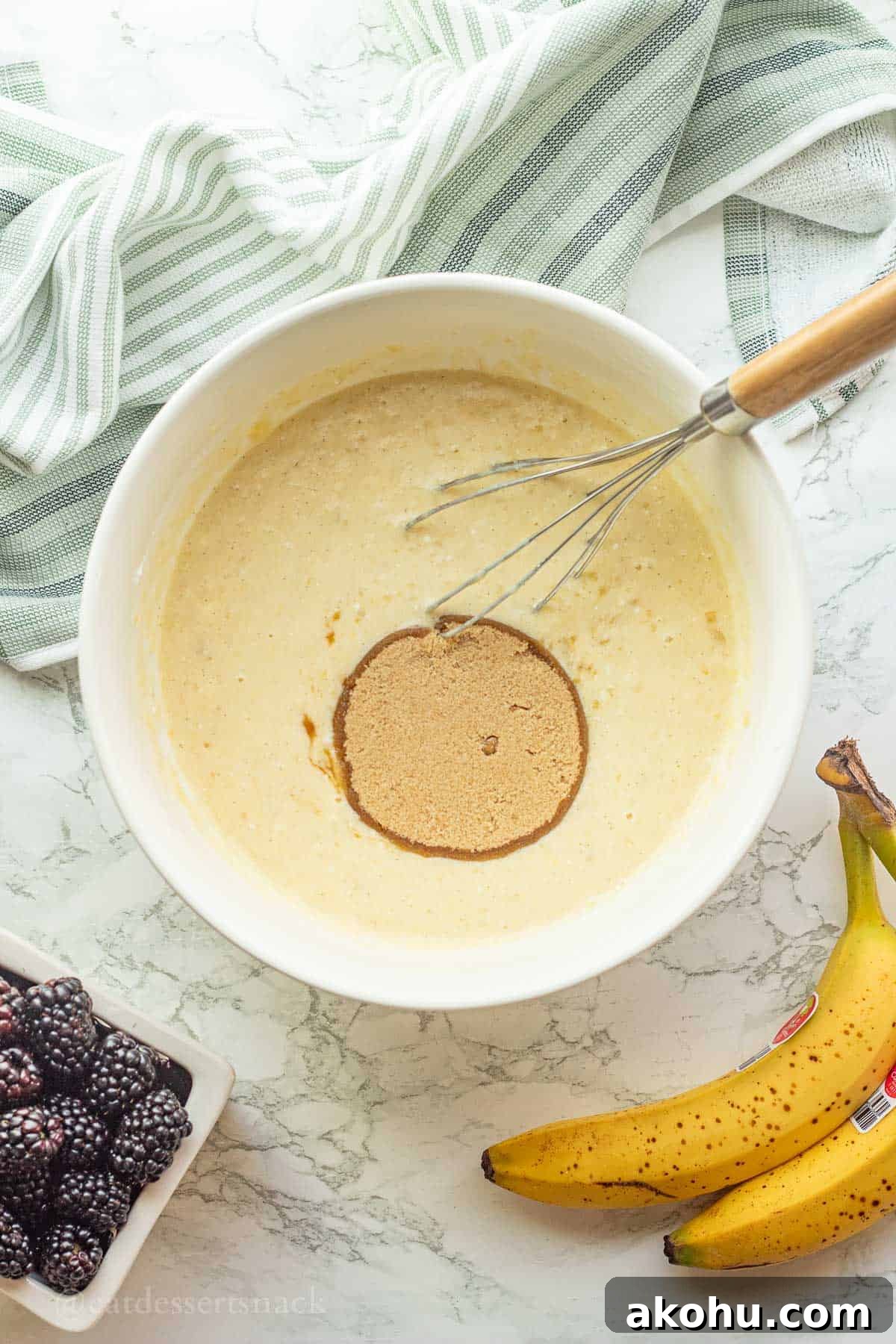 Banana Blackberry Oatmeal Muffins Recipe — Quick Baked Breakfast 6 Brown sugar in raw muffin batter in white bowl with whisk.