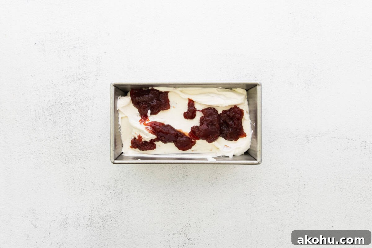 Cream cheese ice cream poured into a loaf pan, with strawberry jam added on top.