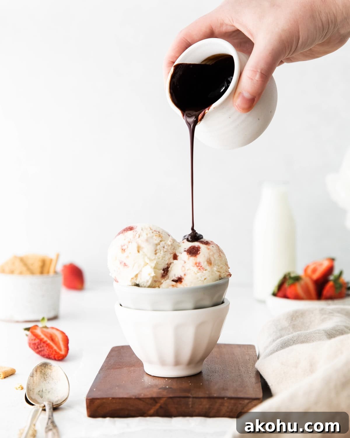 Pouring chocolate sauce over scoops of strawberry cream cheese ice cream in a bowl.