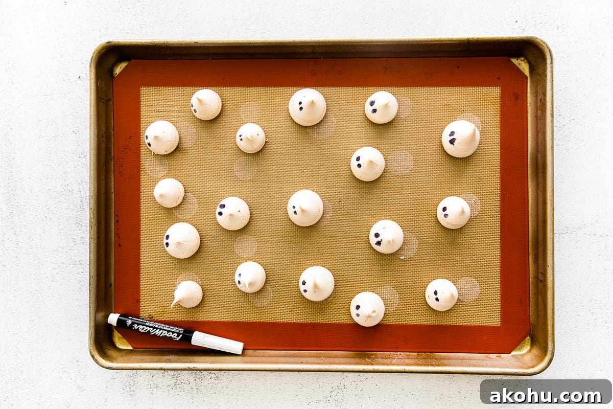 How to Make Adorable Meringue Ghosts for Halloween Treats 12 Ghost meringues lined up on a baking sheet, dotted with eyes.