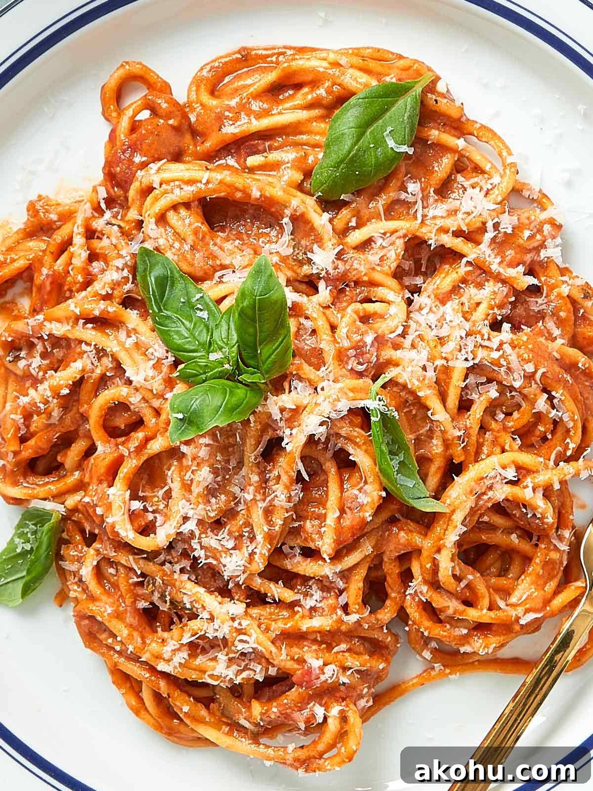Close-up of a plate of creamy tomato pasta with fresh basil and parmesan served in a white dish.