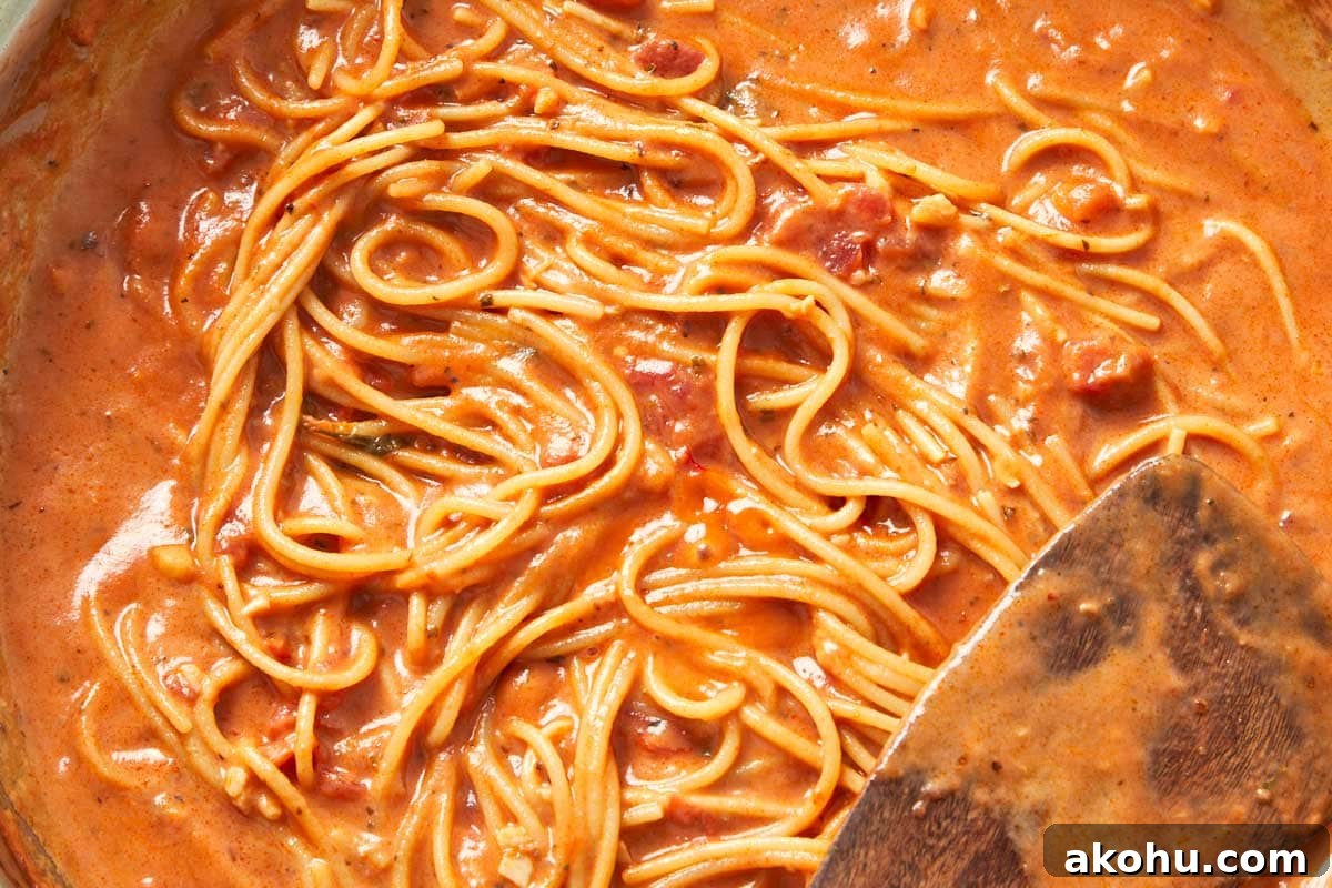 Cooked creamy tomato pasta being plated in generous swirls, rich and velvety.