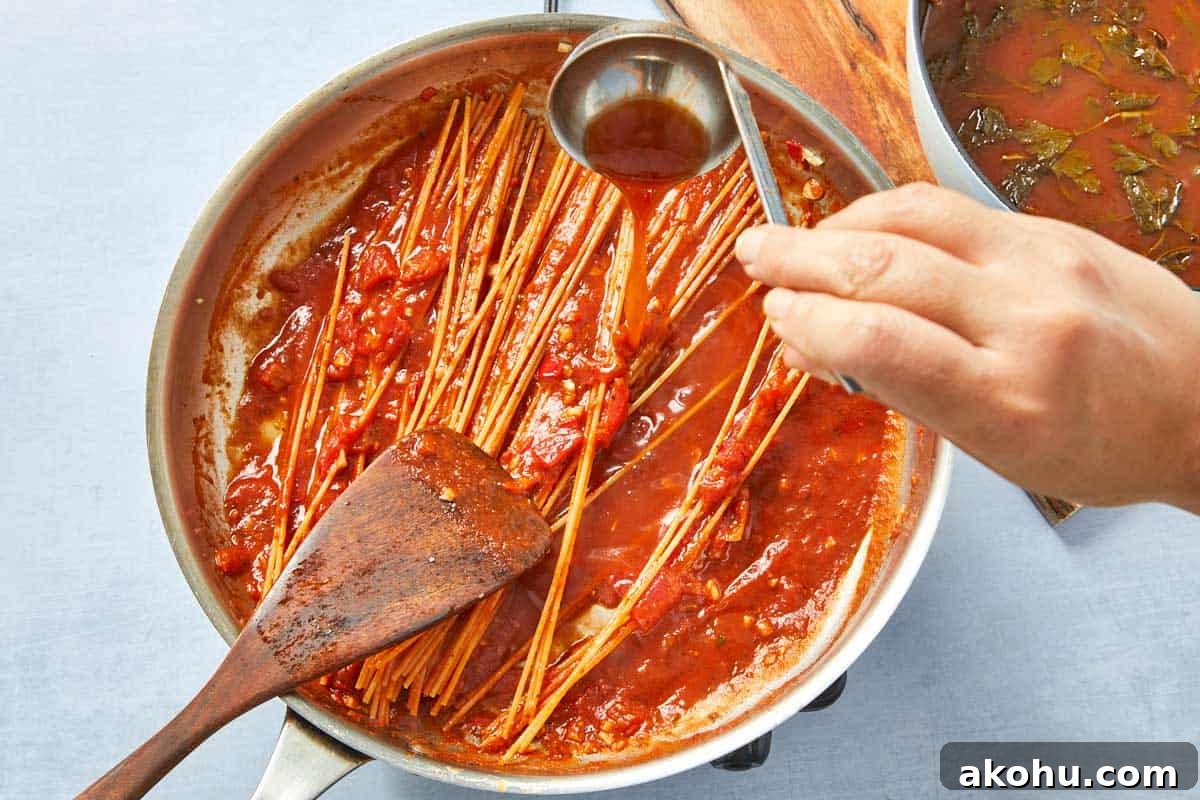 Warm broth being added spoonful by spoonful to the tomato pasta, slowly absorbed.