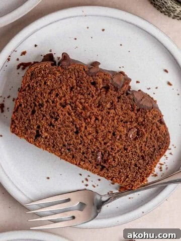 A slice of chocolate loaf cake with chocolate chips on a plate with a fork.