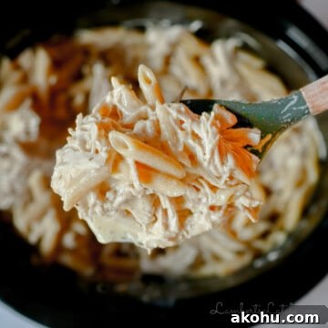 spoonful of crockpot olive garden chicken pasta held above a slow cooker.