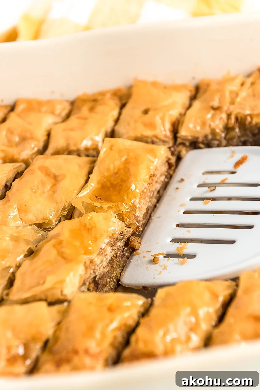 Authentic Homemade Baklava Recipe for Crispy Layers 6 Spatula scooping pieces of baklava out of a baking dish.